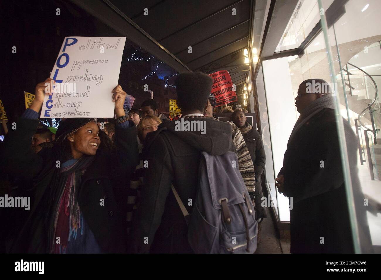 A protester holding a sign passes by a luxury store guarded by a security officer as fellow protesters walk up Madison Ave during a demonstration against the police in the Manhattan borough of New York December 23, 2014. Mayor Bill de Blasio's attempts to soothe a city dismayed by the slaying of two officers were further rebuffed on Tuesday as protesters defied his call to suspend what have become regular demonstrations over excessive police force. REUTERS/Carlo Allegri (UNITED STATES - Tags: CRIME LAW CIVIL UNREST) Stock Photo