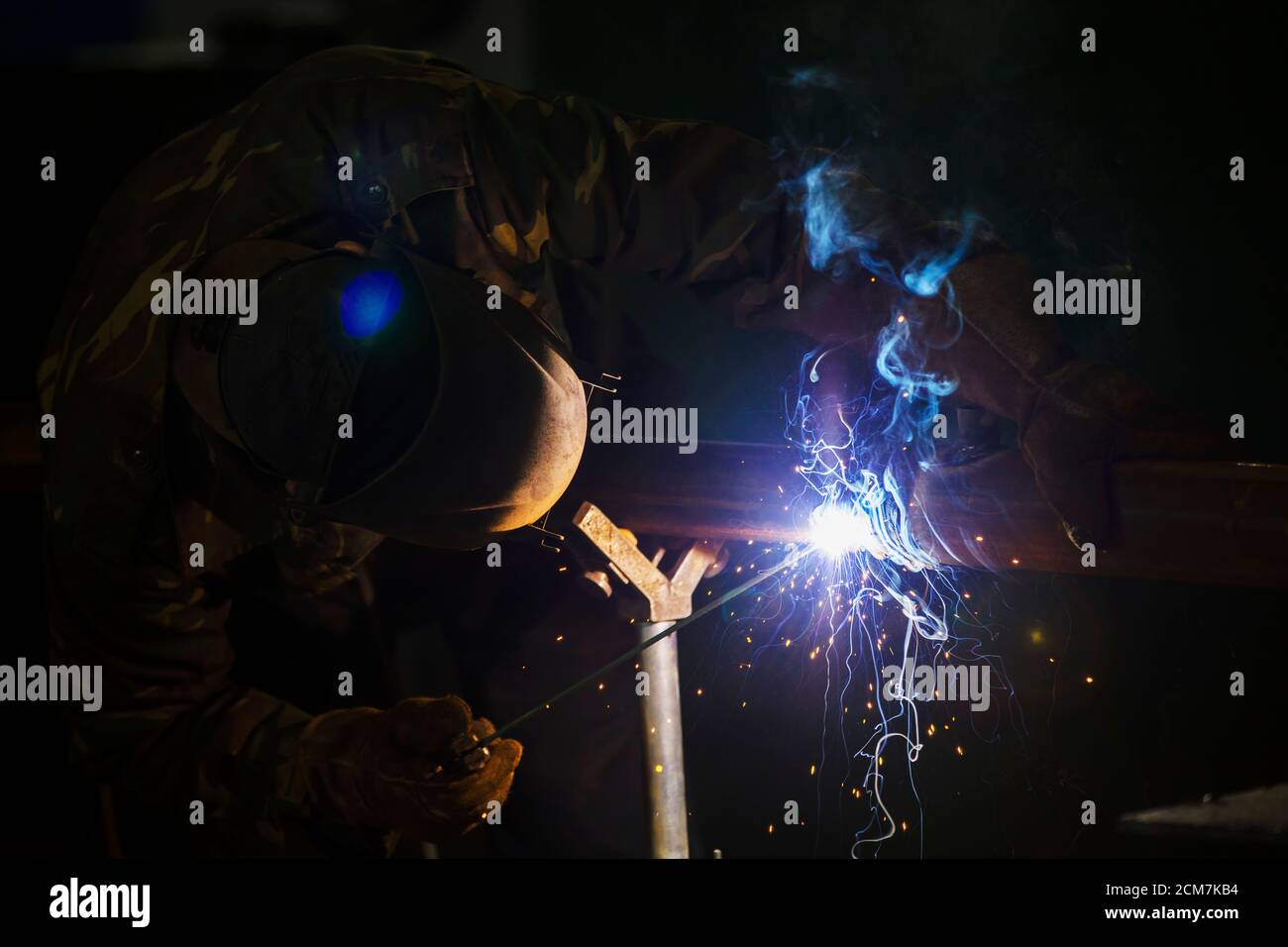 Welder at work. Man in a protective mask. The welder makes seams on the metal. Sparks and smoke when welding. Stock Photo