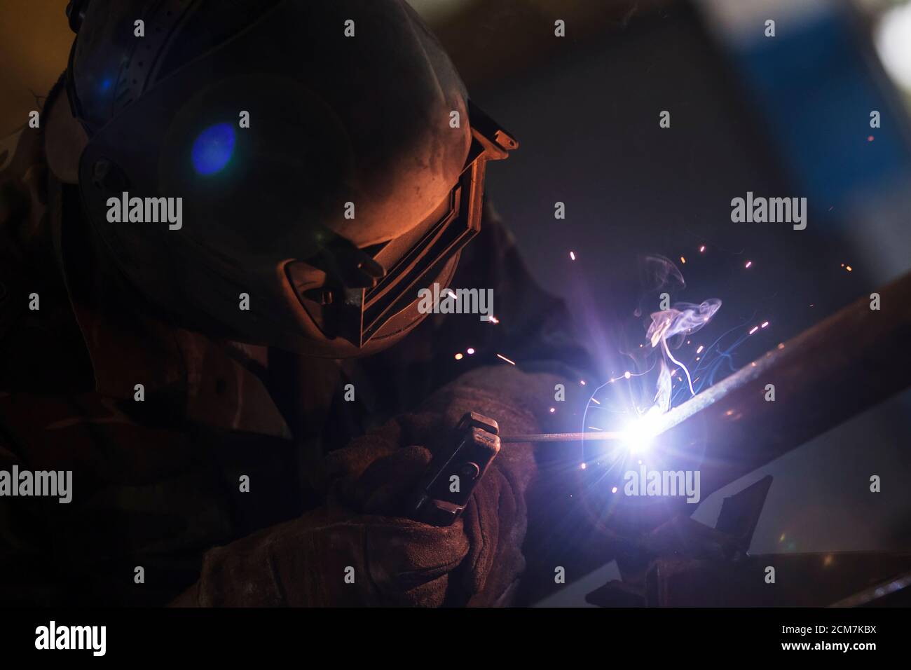 Welder at work. Man in a protective mask. The welder makes seams on the metal. Sparks and smoke when welding. Stock Photo