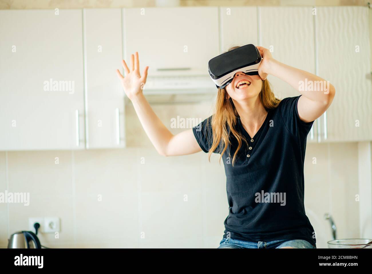 Pretty casual worker using virtual reality headset in her kitchen. Stock Photo