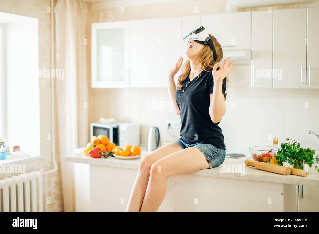 Pretty casual worker using virtual reality headset in her kitchen. Stock Photo