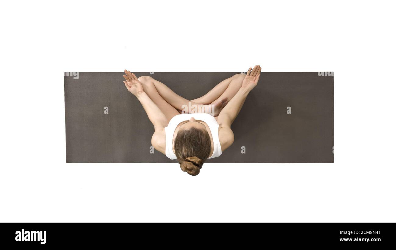 Young woman sitting in lotus pose and meditating on white background ...