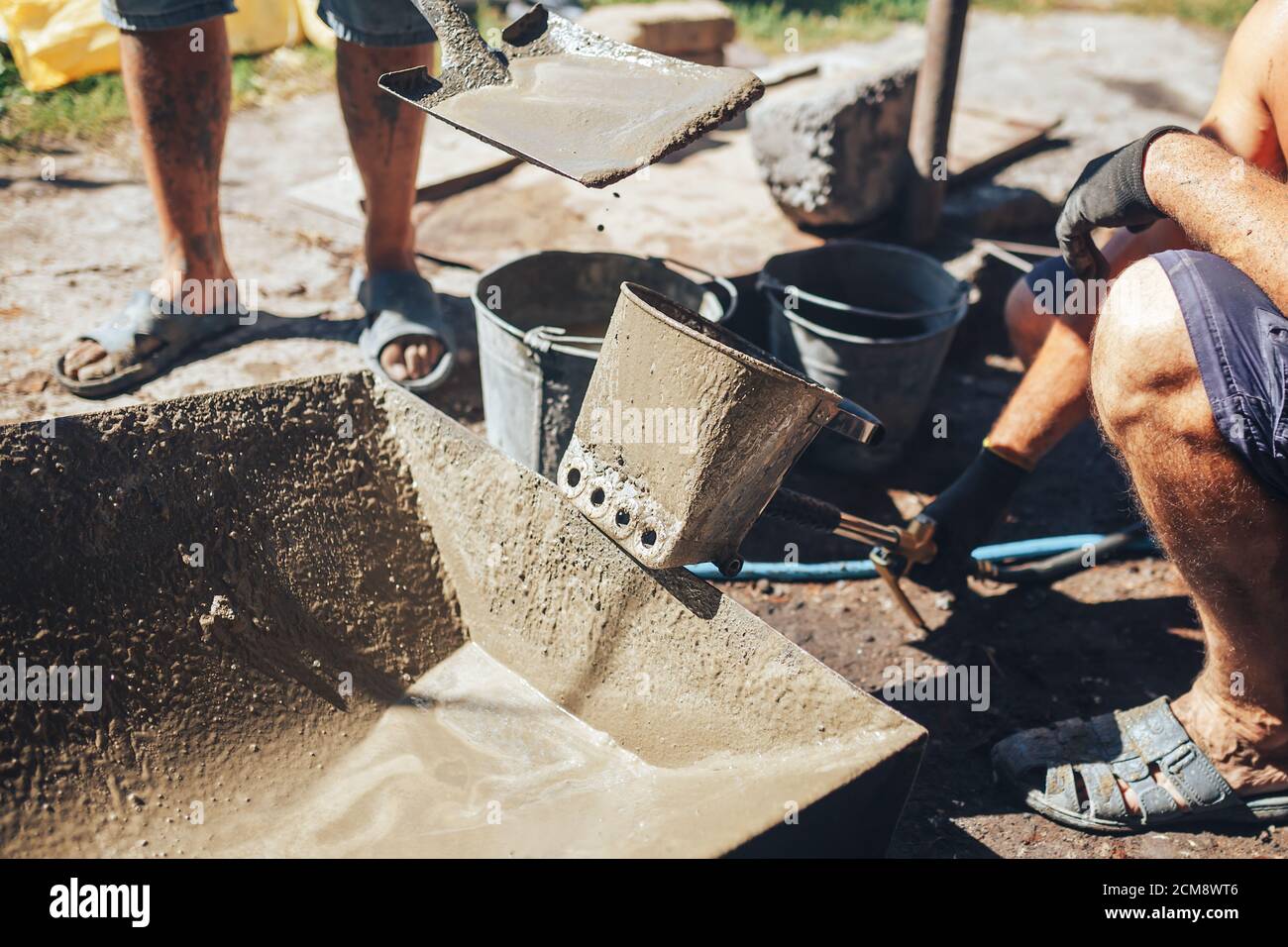 Workers work with cement mortar, loading the hopper bucket with mortar