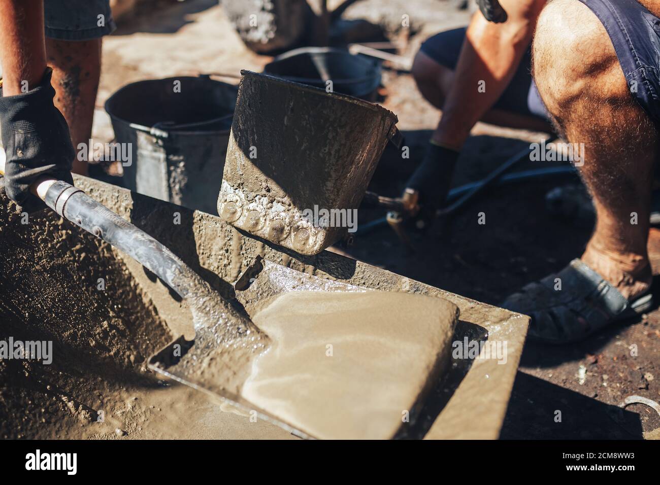 Workers work with cement mortar, loading the hopper bucket with mortar