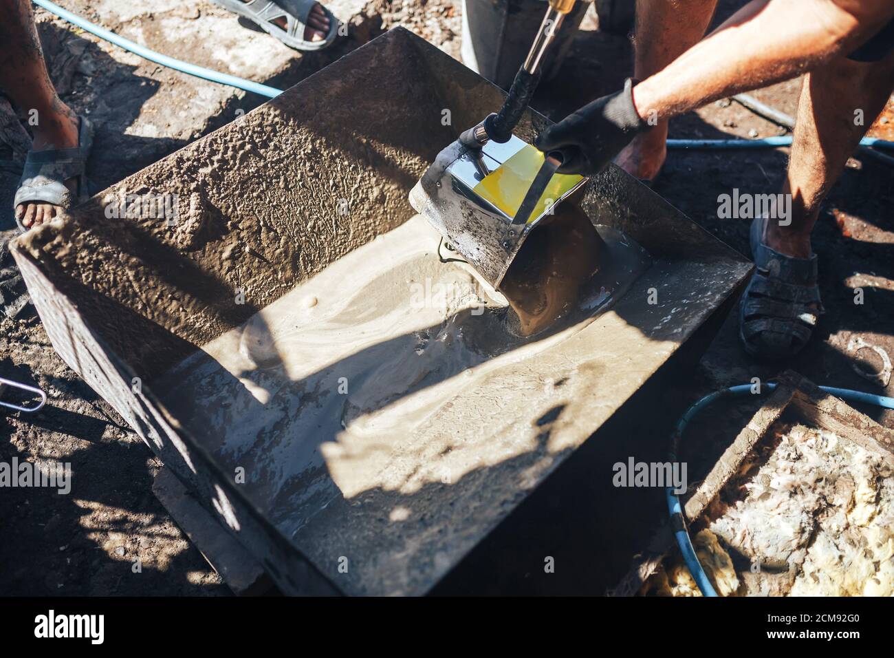 Workers work with cement mortar, loading the hopper bucket with mortar