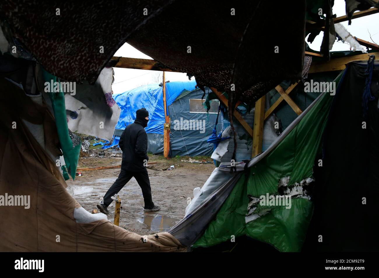A migrant walks past makeshift shelters during the partial dismantelment of the camp for migrants called the 'Jungle' in Calais, France, March 1, 2016.   REUTERS/Pascal Rossignol Stock Photo