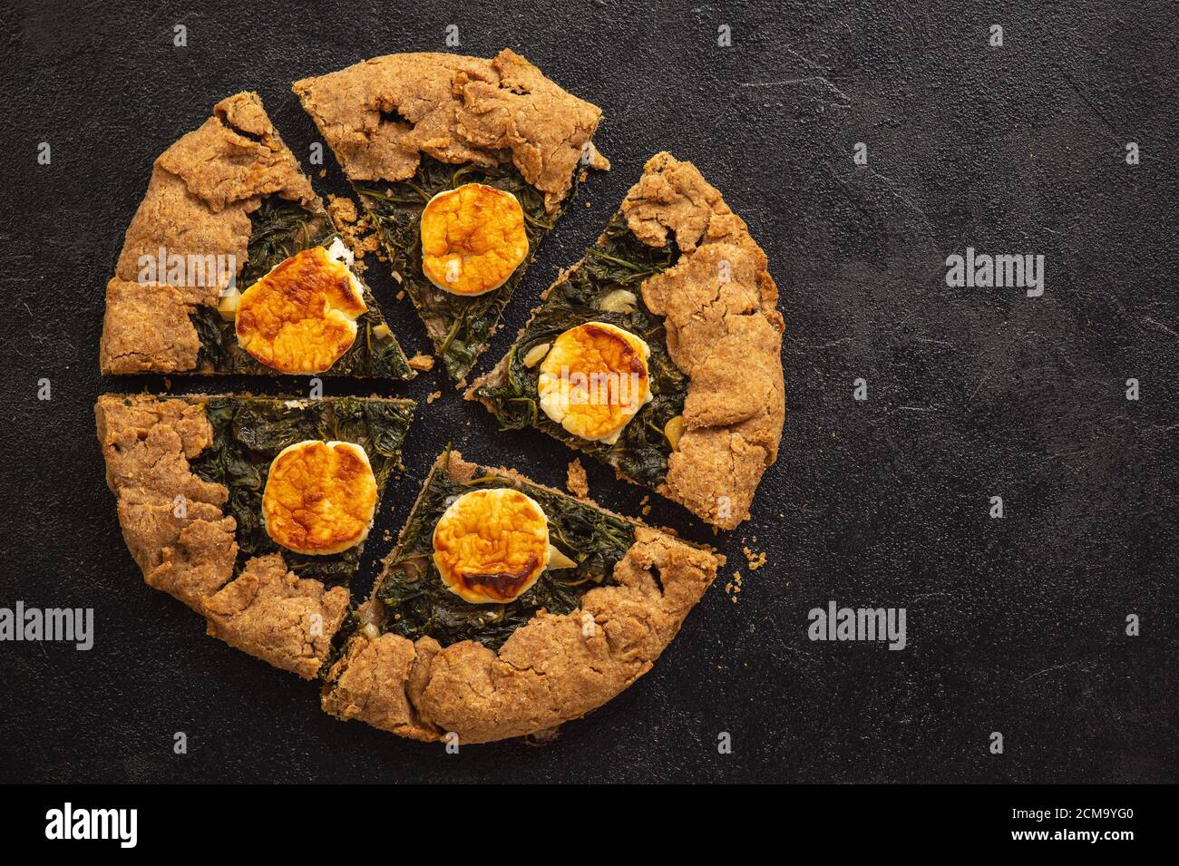 Rustic spinach and goat cheese galette on black background. Stock Photo