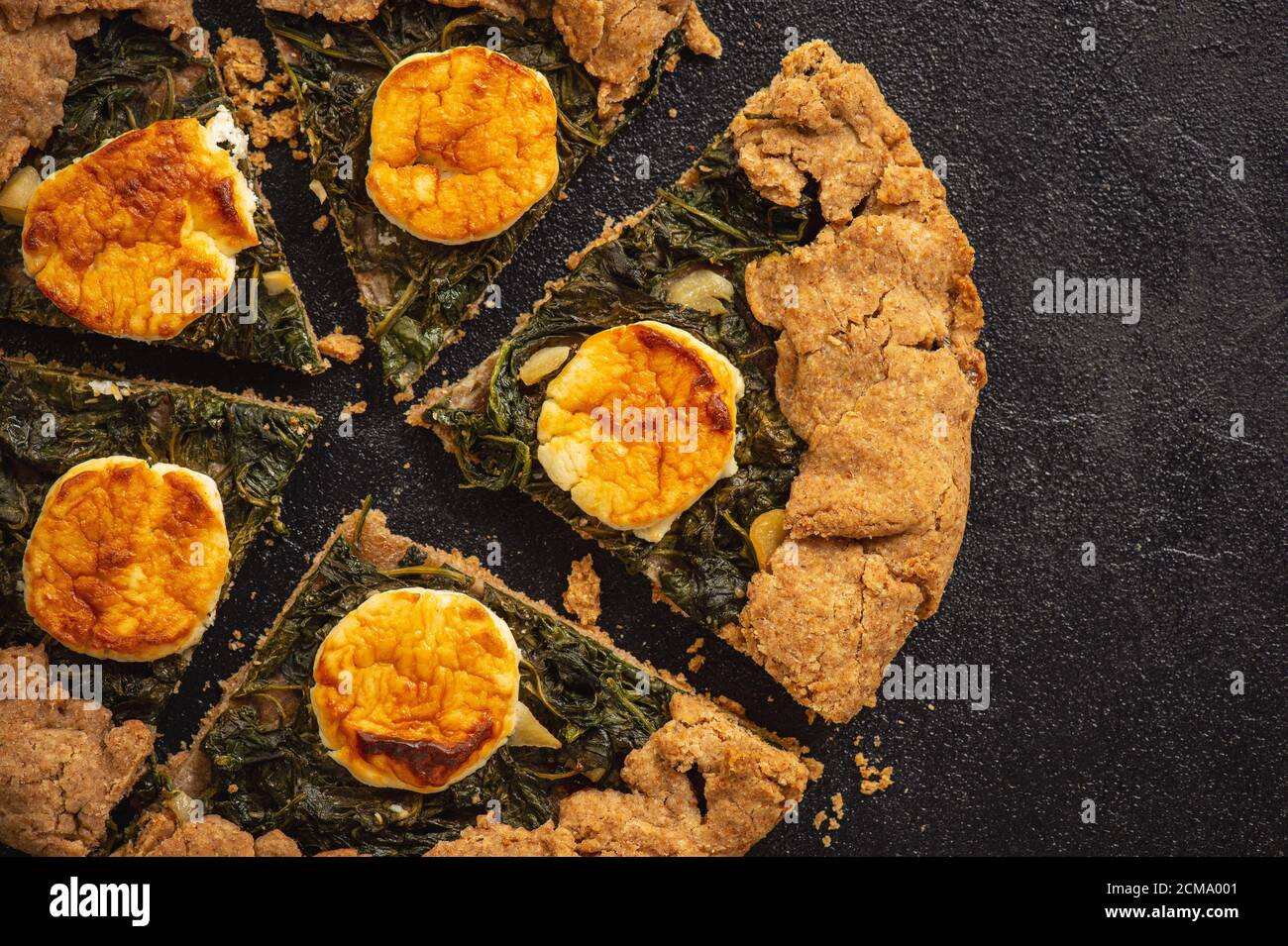 Rustic spinach and goat cheese galette on black background. Stock Photo