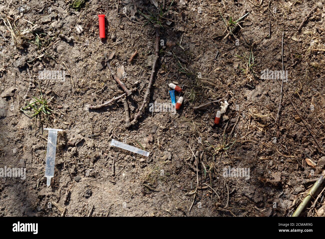 a used broken medical needle, syringe, red cap and pills lie on the ground in a city Park. the danger of addiction Stock Photo