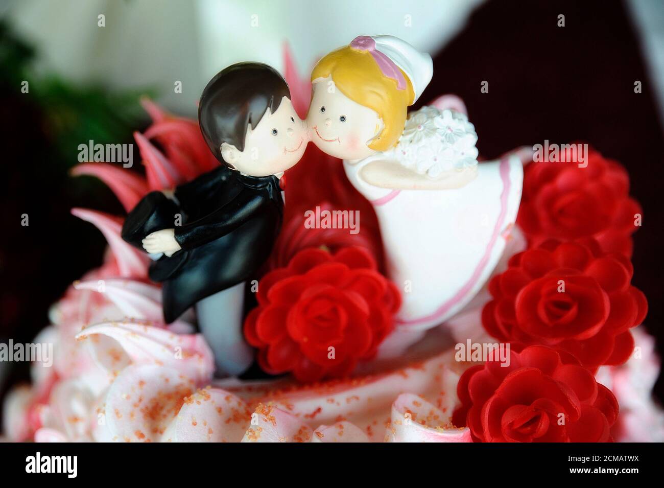 Cute wedding cake topper with bride and groom cheek to cheek or kissing, romantic addition to the colorful special cake, sweet and playful decoration Stock Photo