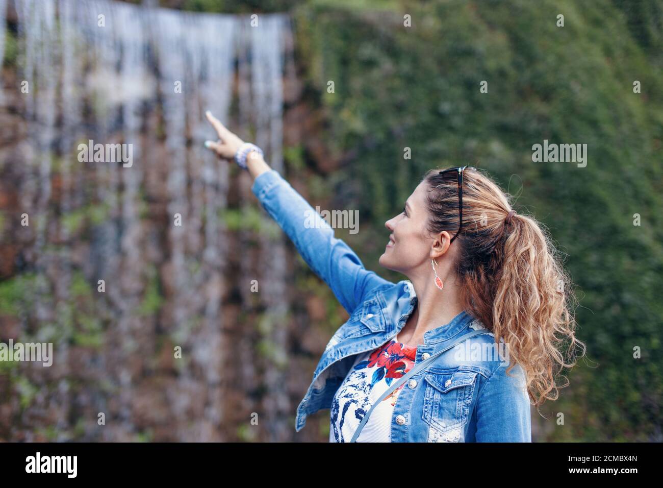 Young 30s trendy woman pointing to waterfall during trip Stock Photo