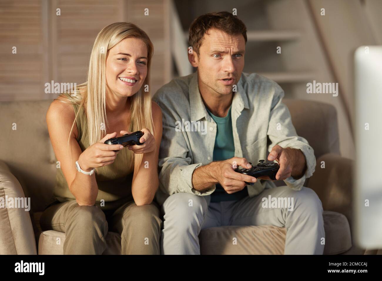 Young smiling couple having fun while playing in computer game at home Stock Photo