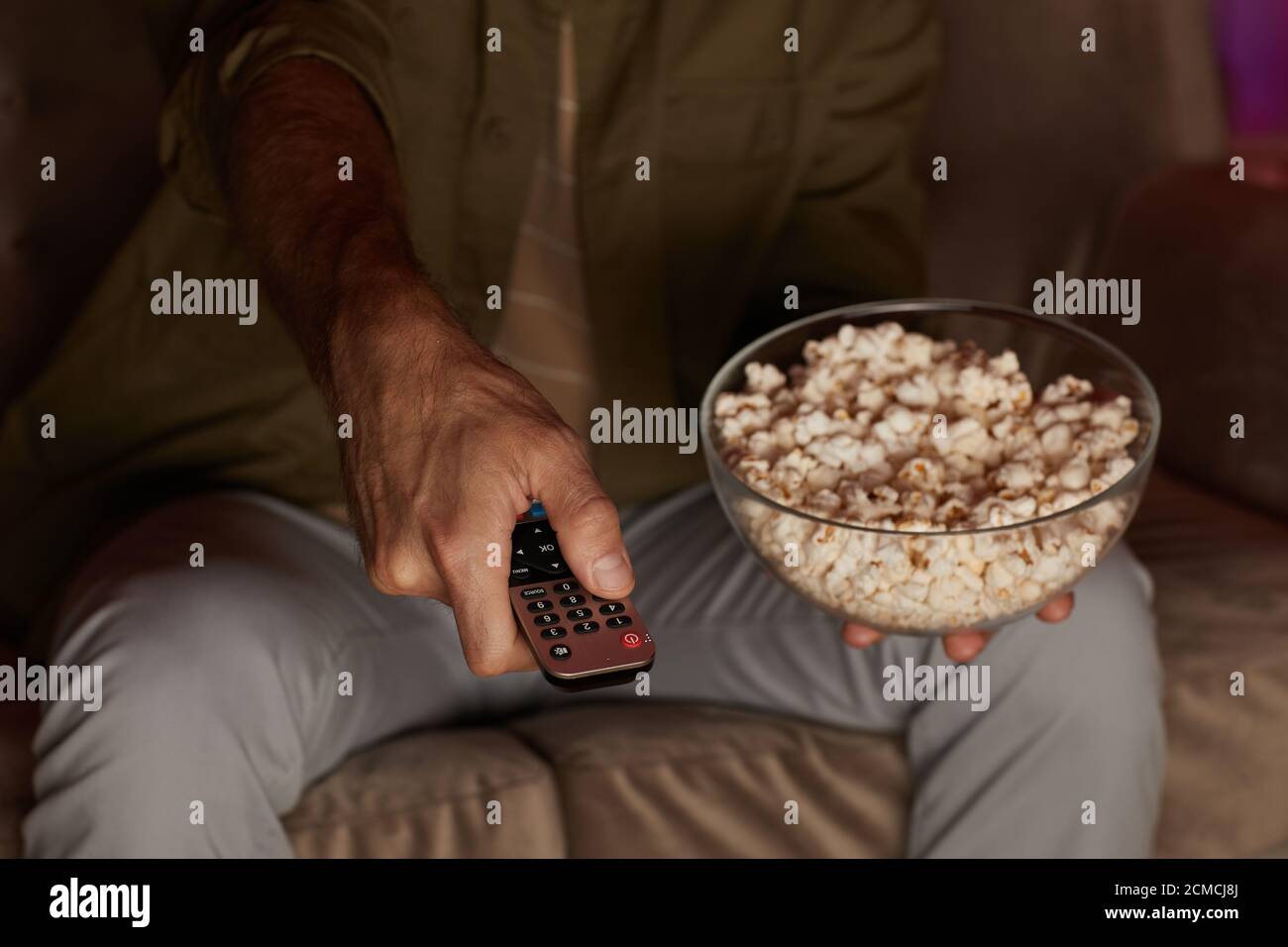 Close-up of man changing channels on TV while watching TV and eating popcorn Stock Photo