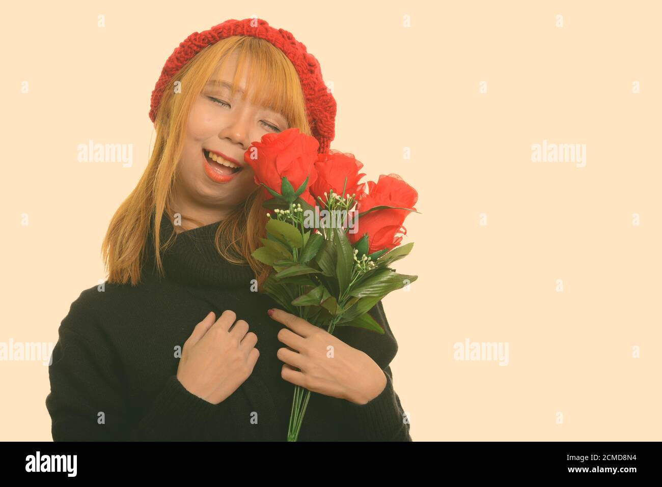 Young happy Asian woman smiling with eyes closed holding red roses ...