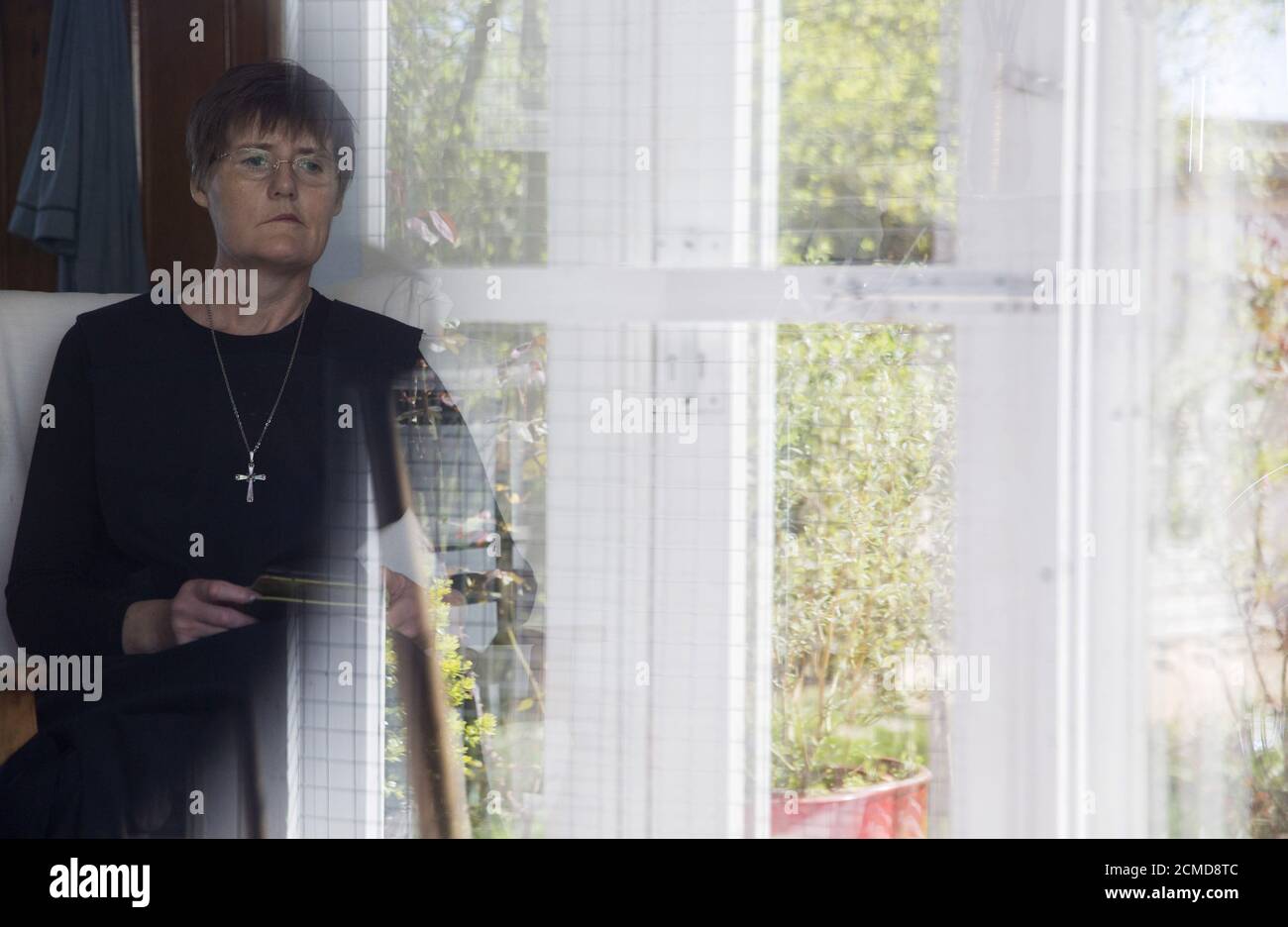 Sister Rachel Denton looks out of a window at St Cuthbert's Hermitage in Lincolnshire, north east Britain April 27, 2015. Denton, a Catholic hermit, rises early to tend to her vegetable garden, feed her cats and pray. But the former Carmelite nun, who in 2006 pledged to live the rest of her life in solitude, has another chore - to update her Twitter account and check Facebook. 'The myth you often face as a hermit is that you should have a beard and live in a cave. None of which is me,' says the ex-teacher. For the modern-day hermit, she says social media is vital: 'tweets are rare, but preciou Stock Photo