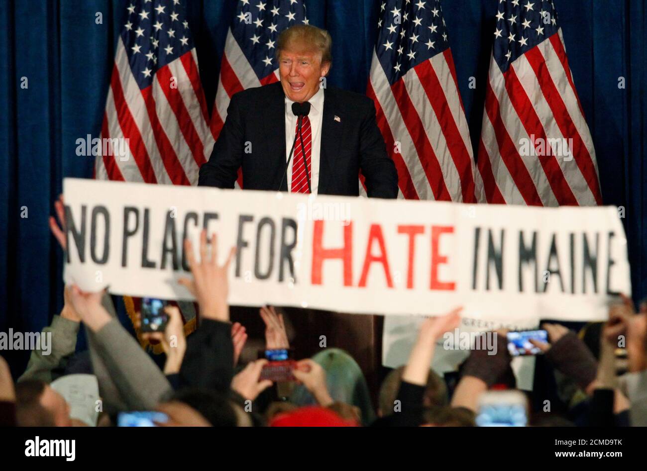Republican U.S. presidential candidate Donald Trump smiles as protestors hold up a sign reading 'No Place for Hate in Maine' during a campaign rally in Portland, Maine March 3, 2016. REUTERS/Joel Page TPX IMAGES OF THE DAY Stock Photo