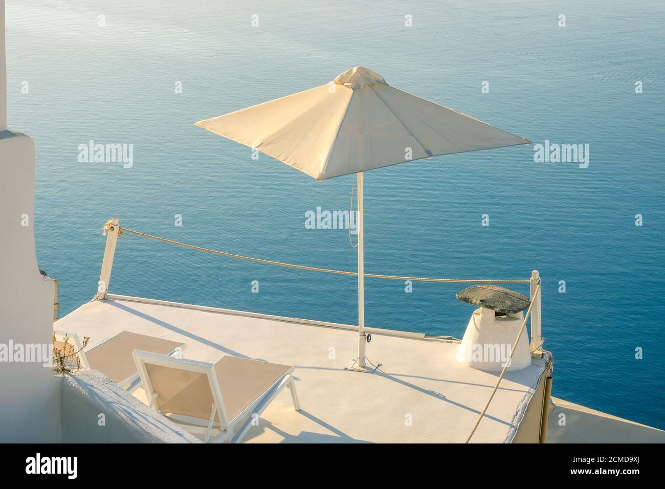 Greece. A quiet summer evening in Santorini. Two sun loungers and an umbrella on the balcony with a sea view Stock Photo