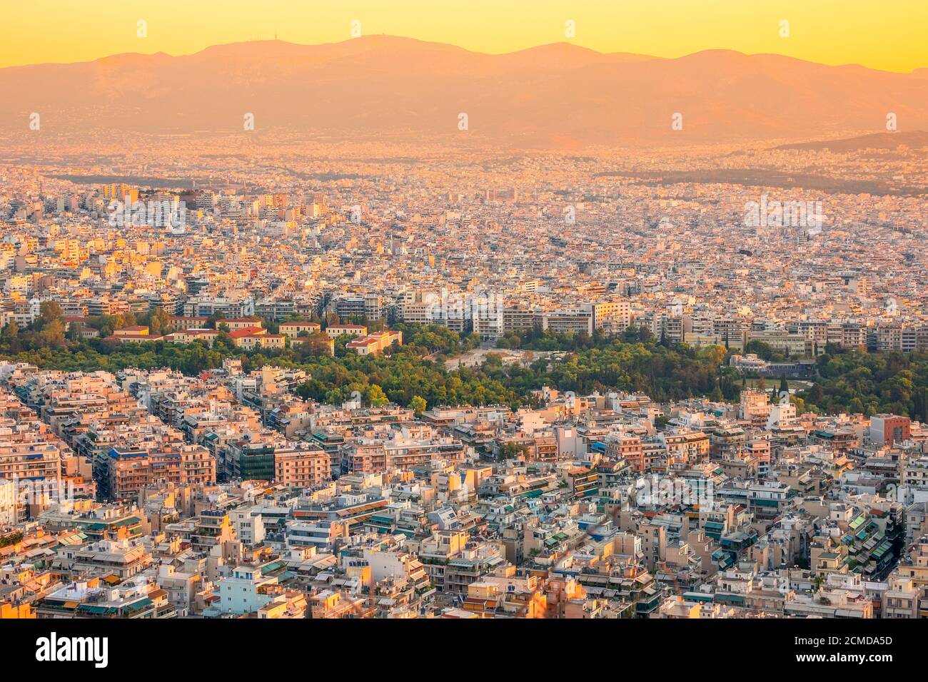 Greece. Warm summer evening over the rooftops of Athens. Residential and office buildings and narrow streets. Green parks. Aerial view Stock Photo