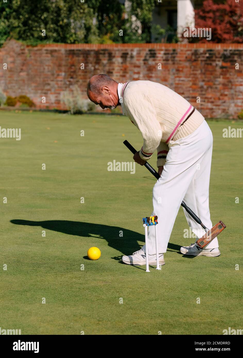 A man dressed in traditional whites playing lawn croquet holding a croquet mallet next to a hoop with clips on a summers day in the UK - summer sport Stock Photo
