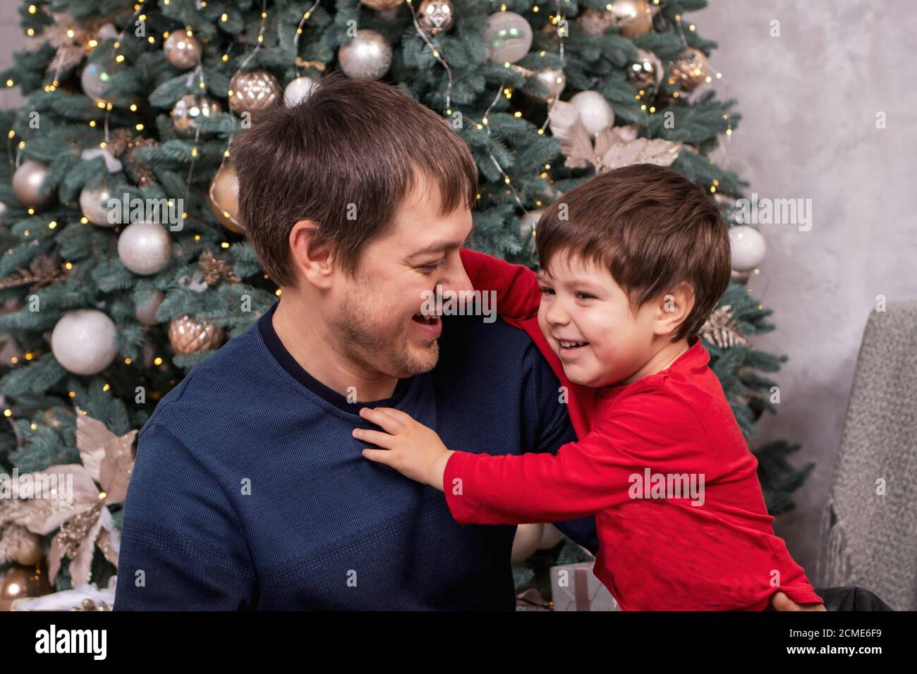 Dad and son have fun, laugh and smile around the Christmas tree. New Year's Eve. Stock Photo