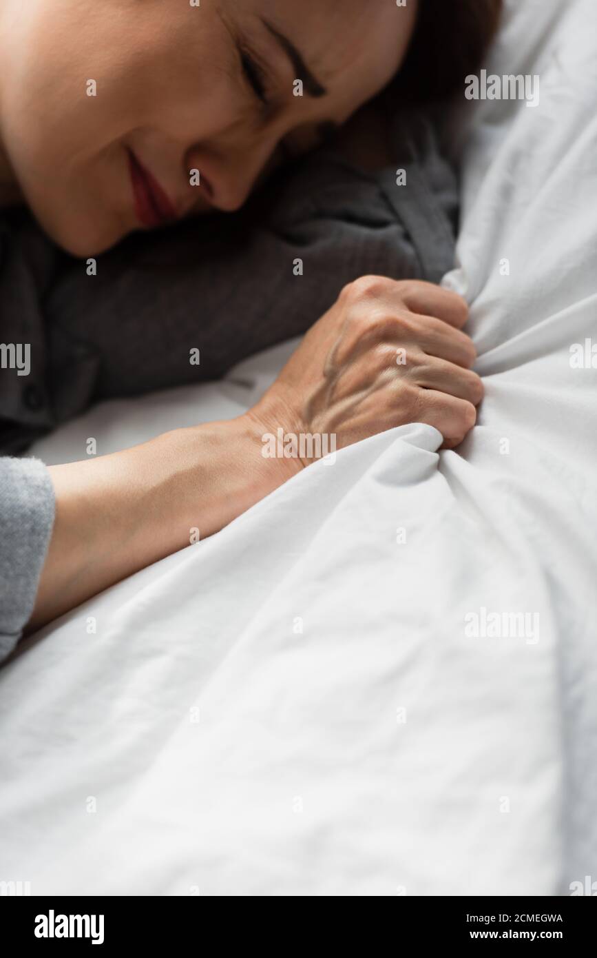 Top View Of Frustrated And Brunette Woman Touching Bedding While Crying top-view-of-frustrated-and-brunette-woman-touching-bedding-while-crying