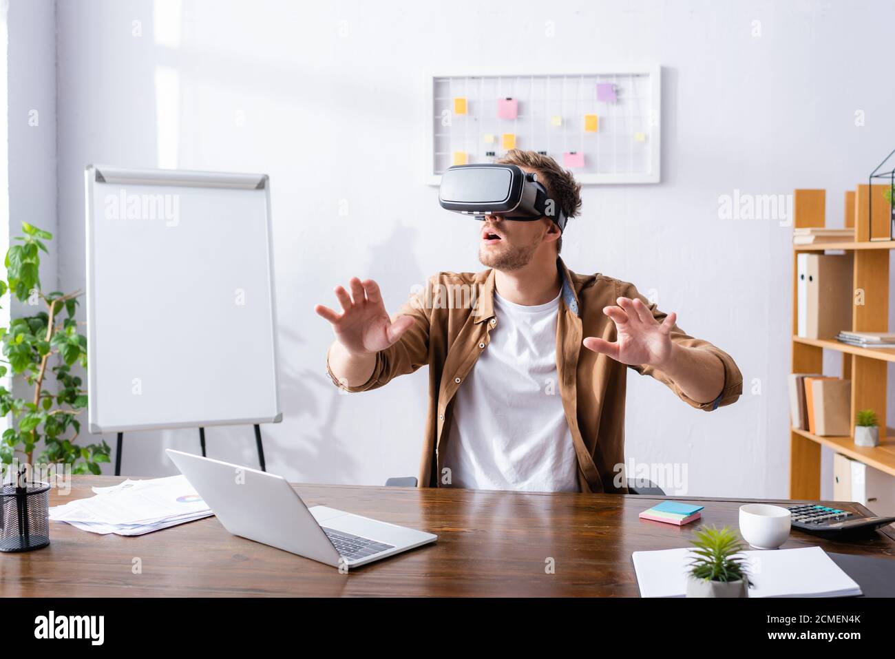 excited businessman gesturing while using vr headset at workplace Stock Photo
