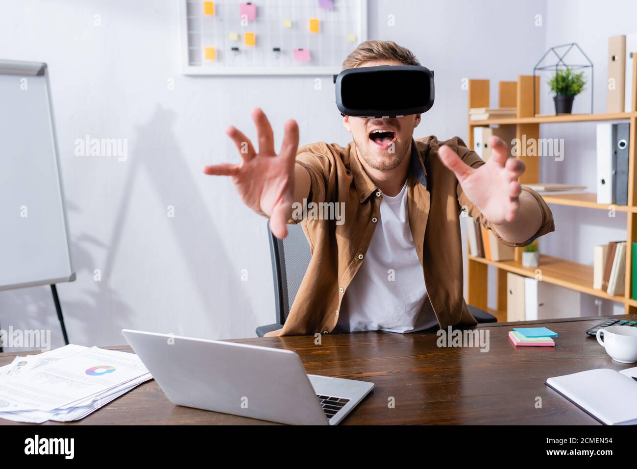 excited businessman in vr headset gesturing near laptop at workplace Stock Photo