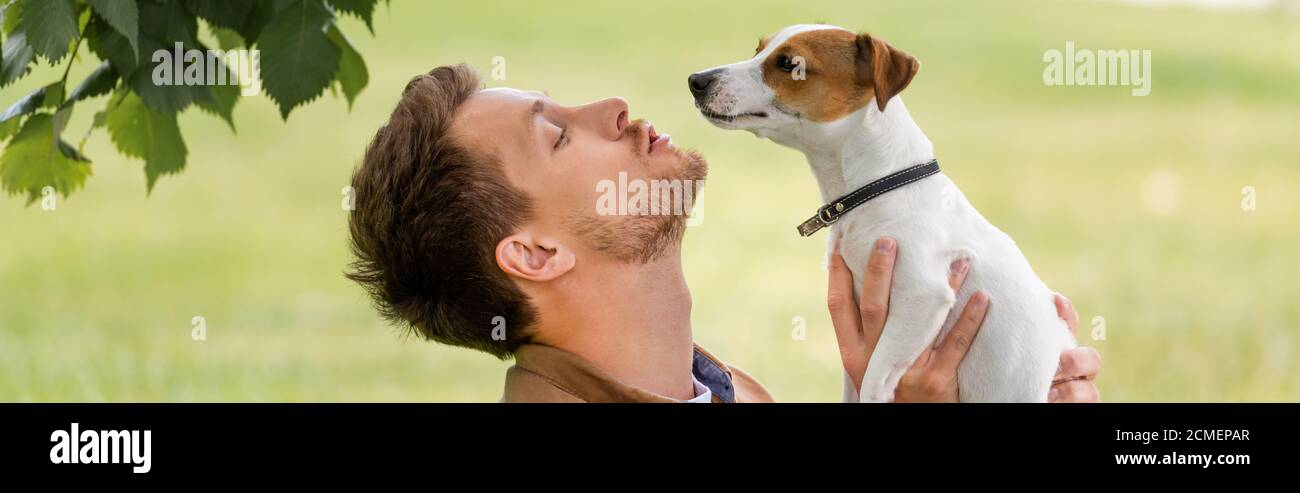 horizontal concept of young man holding jack russell terrier dog with brown spots on head Stock Photo