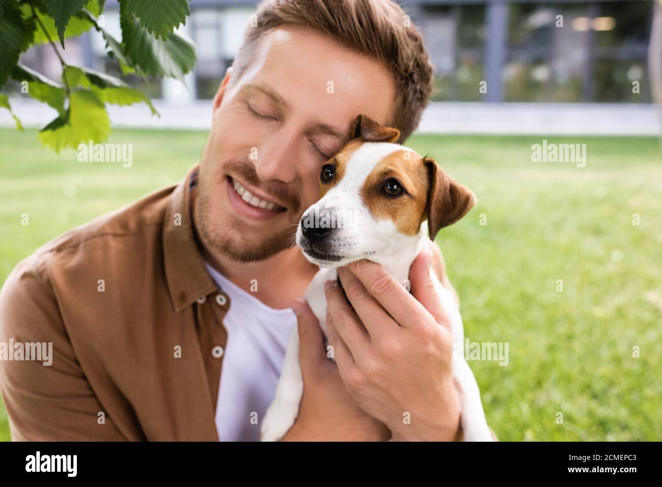 young man with closed eyes holding white jack russell terrier dog with brown spots on head Stock Photo