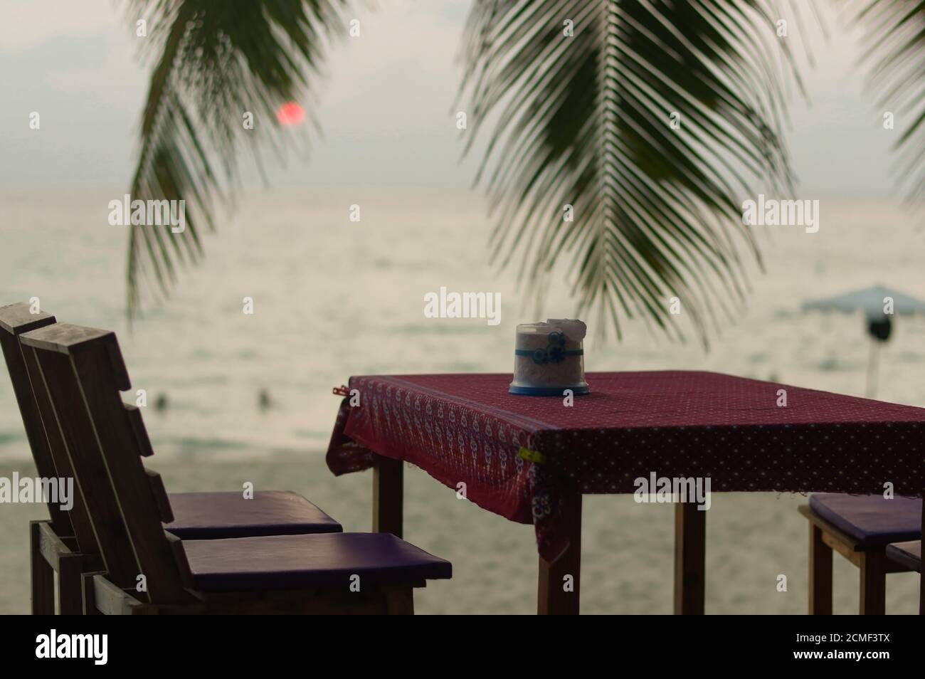 romantic outdoor restaurant table and chairs at the beach on sunset with plam leaves Stock Photo