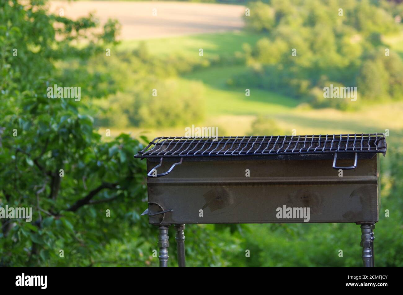 Empty portable BBQ grill in front of a fresh green summer landscape, close-up Stock Photo