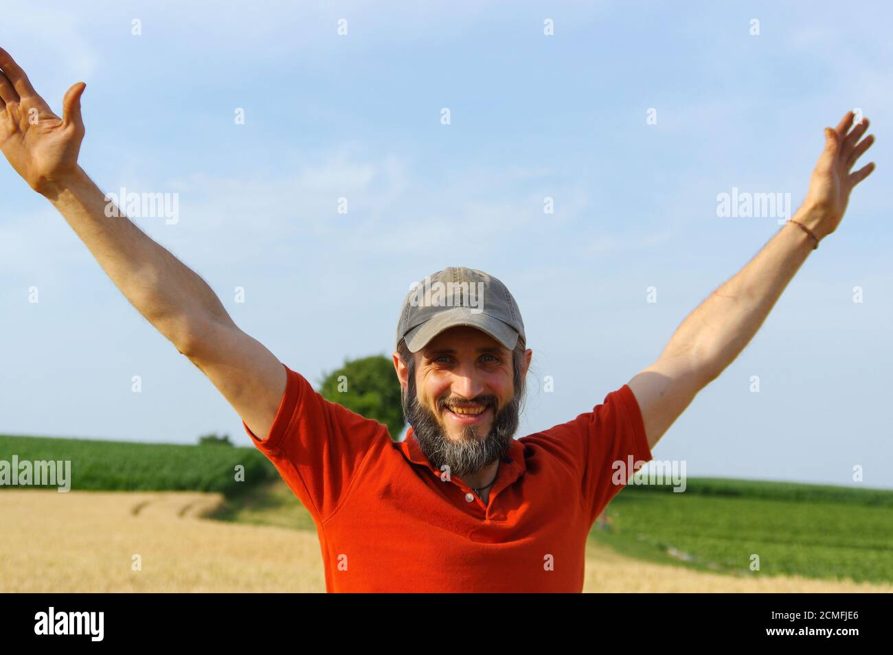 happy bearded man raised up his hands to the sky in a golden summer corn filed, with open arms. Stock Photo