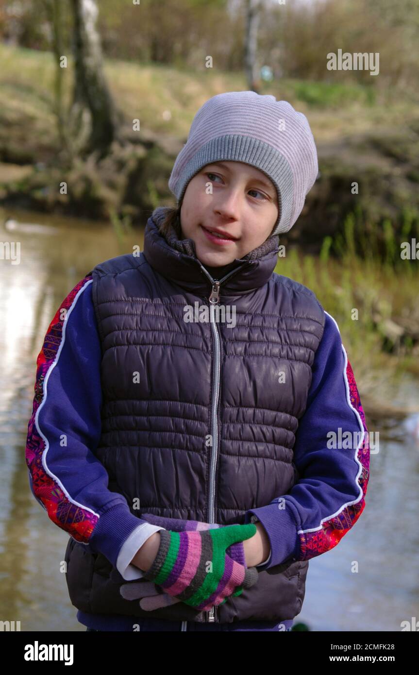 closeup portrait of a standing girl in park near pond in the spring, wearing hat, gloves and folded Stock Photo