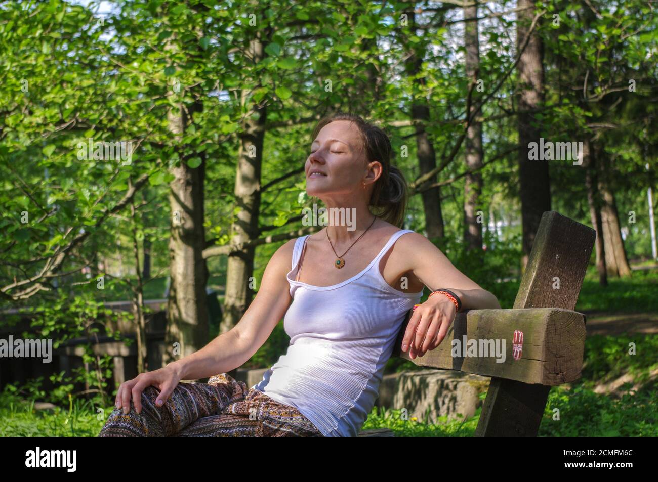 young happy woman sitting outdoors on bench and relaxing with close eyes Stock Photo