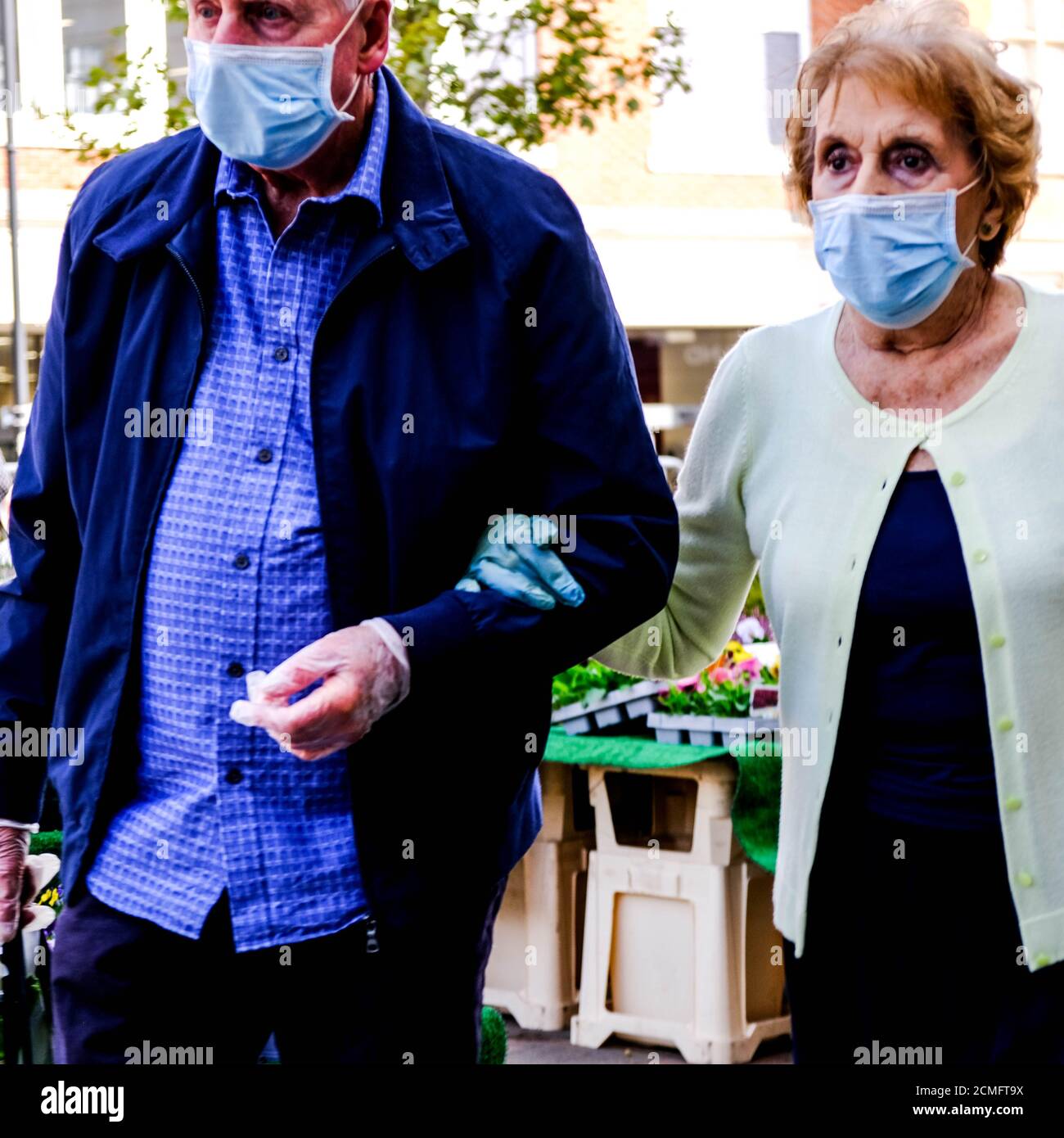 Elderly Couple Walking Arm In Arm Wearing Face Masks During COVID-19 Pandemic Stock Photo