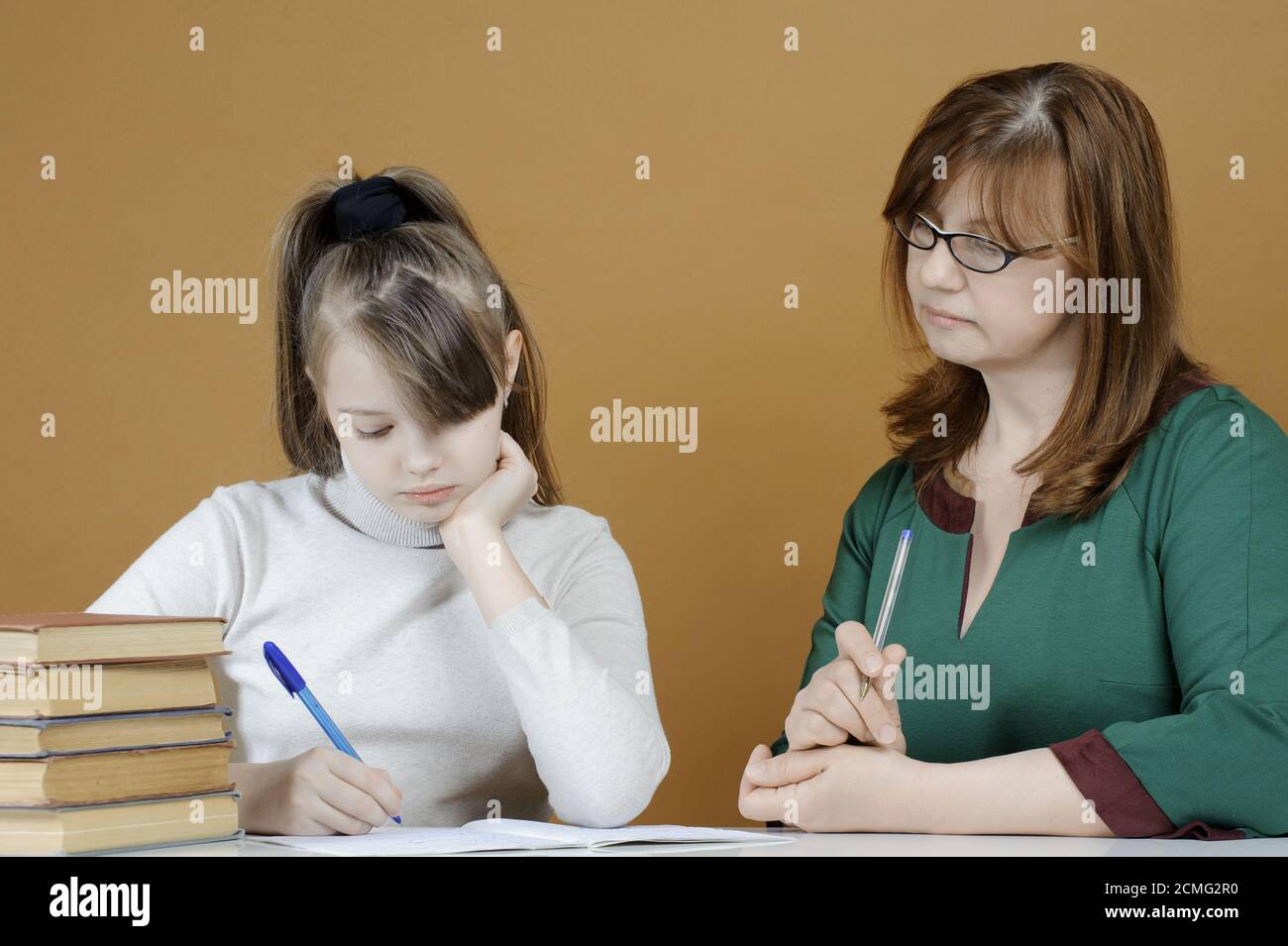 The child makes school lessons under the supervision of her mother. Stock Photo