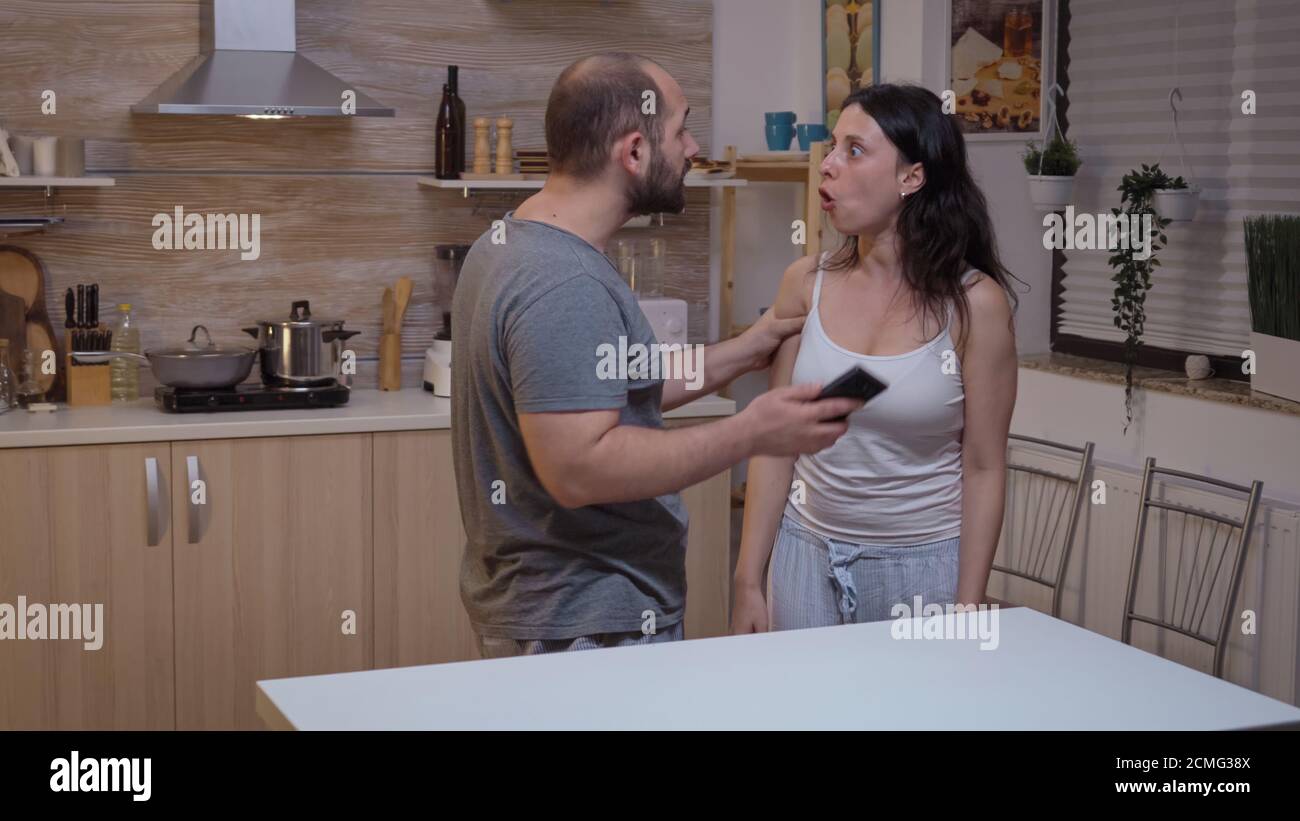 Cheated man yelling at wife and hitting her. Jealous husband angry, frustrated, offended and irritated accusing woman of infidelity arguing her with messages on smartphone screaming desperate Stock Photo
