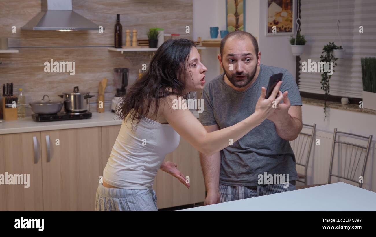 Angry woman yelling at unfaithful man. Jealous wife cheated angry frustrated offended irritated accusing her husband of infidelity showing him messages on smartphone screaming desperate Stock Photo