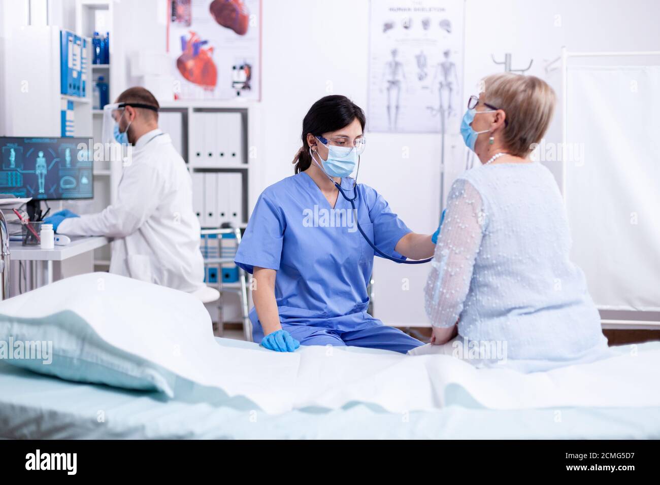 Cardiologist assistant listening heart of senior woman with stethoscope during consultation and wearing face mask against coronavirus outbreak. Medical examination for infections, disease. Stock Photo