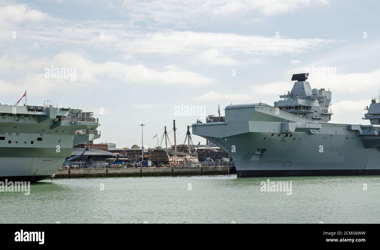 The historic HMS Victory on display at Portsmouth Historic Dockyard viewed between the Royal Navy aircraft carriers HMS Prince of Wales and HMS Queen Stock Photo