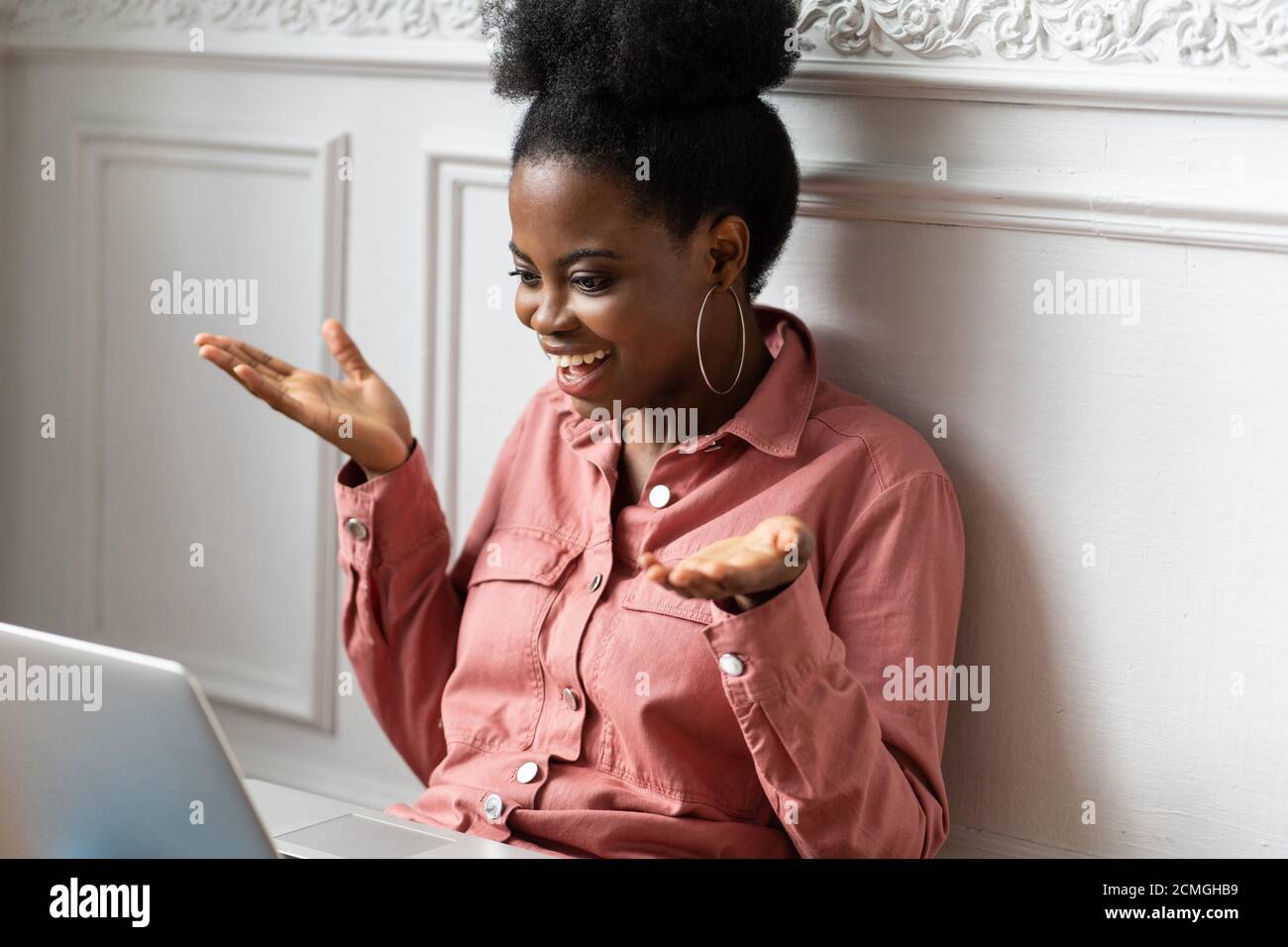 African American millennial biracial woman with afro hairstyle working on laptop, gesturing with hands, looking at camera webcam and chatting and talk Stock Photo
