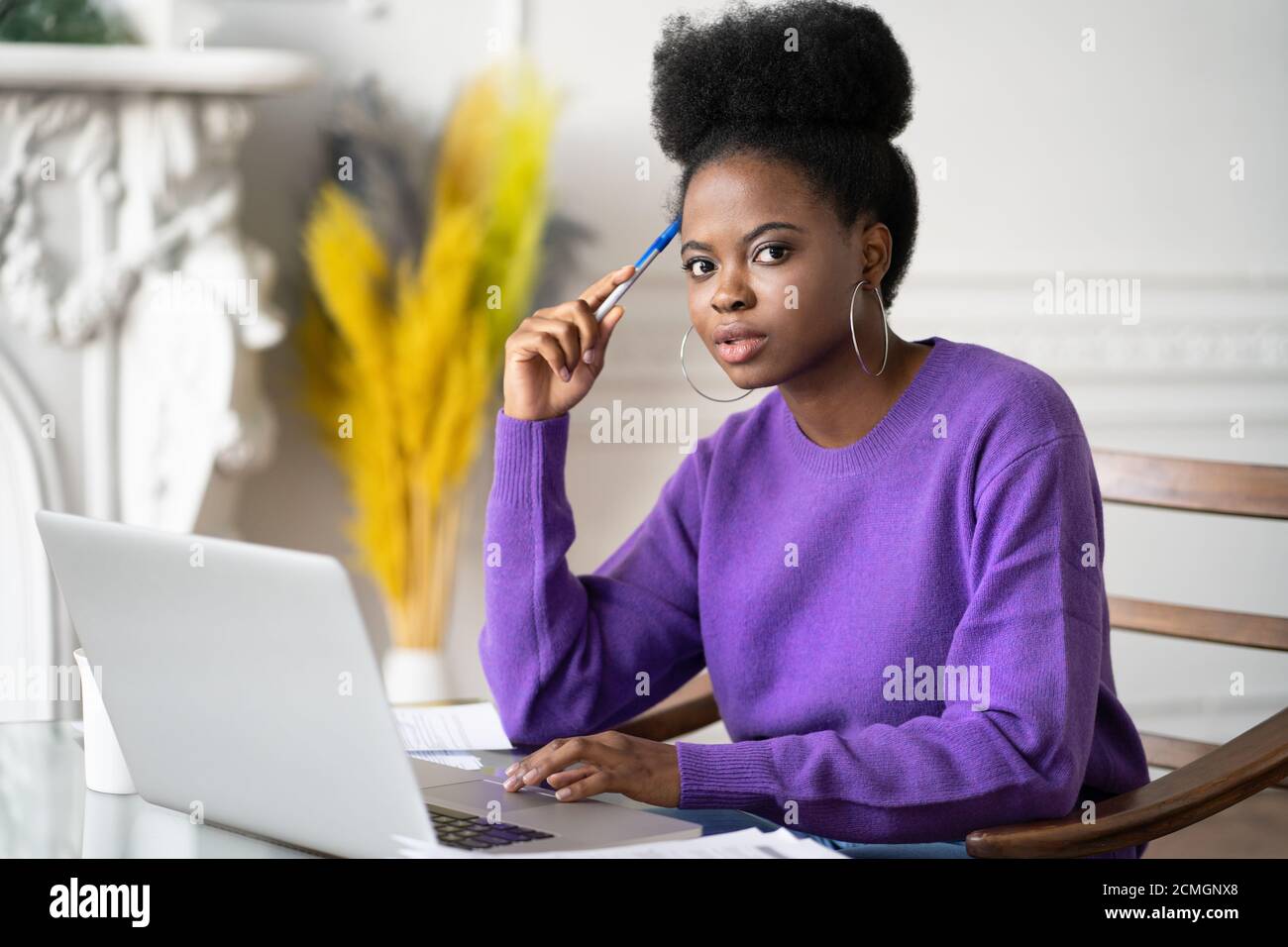 Portrait of Afro-American millennial student woman with afro hairstyle looking at camera while making researches browsing information on laptop, prepa Stock Photo