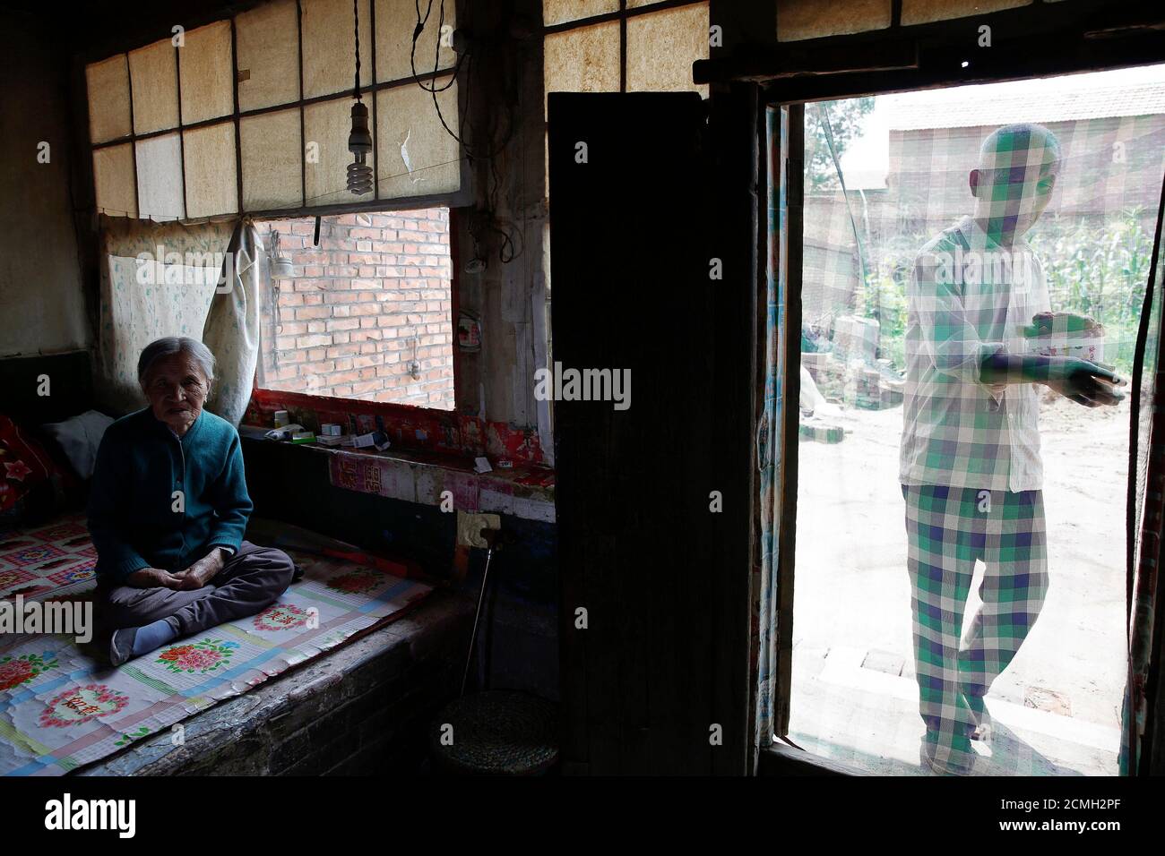 Former Chinese "comfort woman" Zhang Xiantu rests on a traditional brick bed as her son brings her lunch in Xiyan Town, Shanxi Province, China, July 18, 2015. "Comfort women" is the Japanese euphemism for women who were forced into prostitution and sexually abused at Japanese military brothels before and during World War Two. Zhang is the only surviving former "comfort woman" of the 16 plaintiffs in Shanxi who sued the Japanese government in 1995 for abducting girls and using them as "comfort women" during World War Two. According to information from China's Commission of Inquiry into the Fact Stock Photo