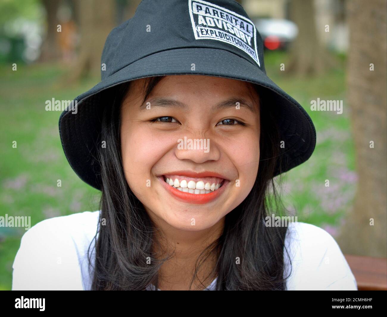 Cheerful Vietnamese girl from Hanoi wears a funny Parental Advisory Explicit Content bucket hat and smiles for the camera. Stock Photo