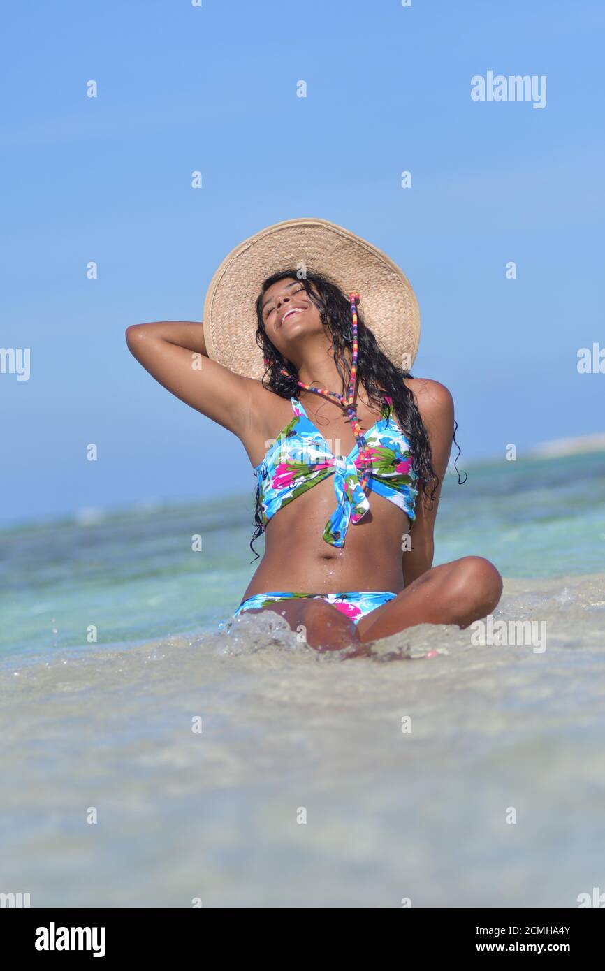 Hispanic woman siting on sand beach laughing with close eyes and splash water. Happiness Stock Photo