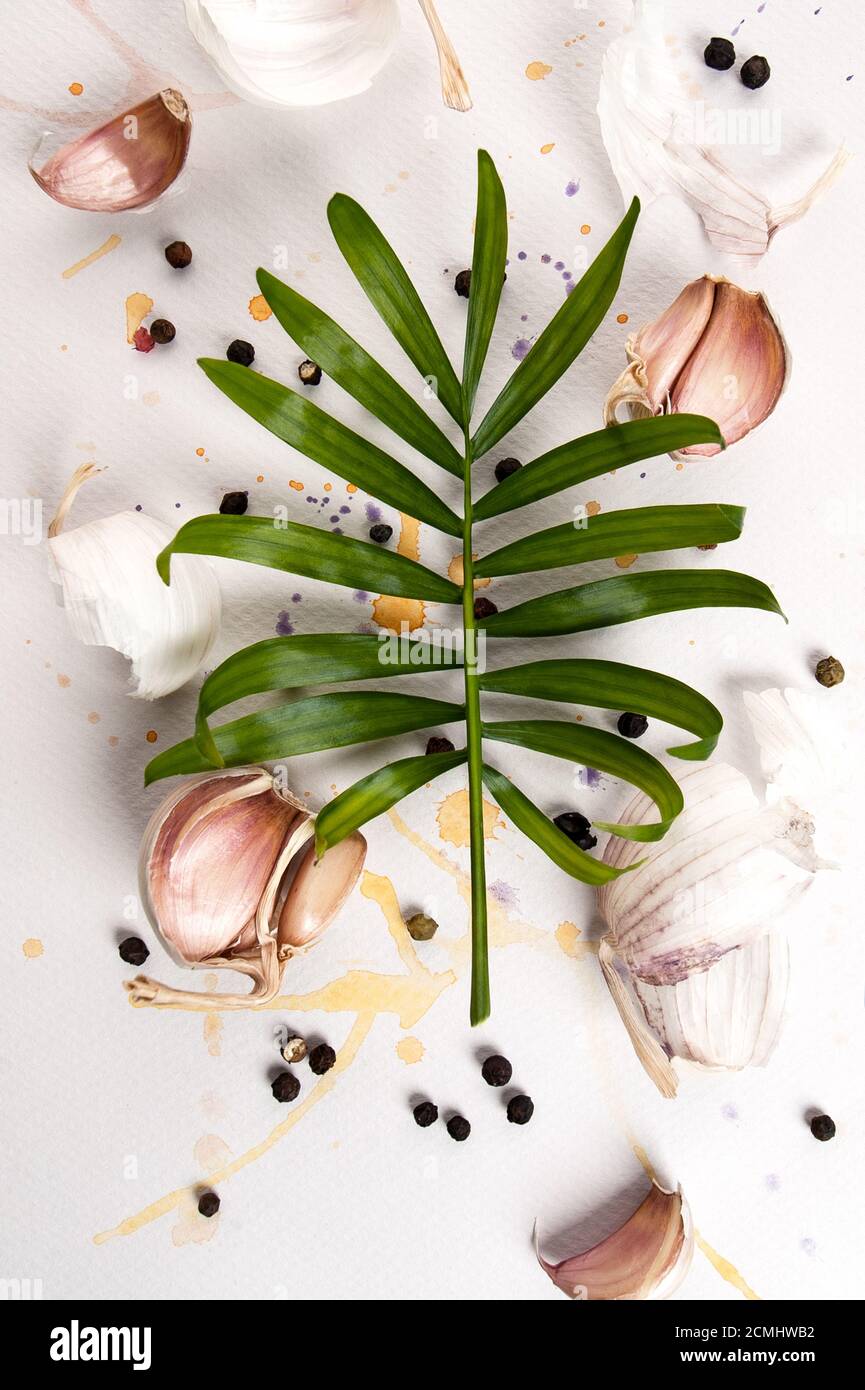 Garlic cloves and a leaf of a tropical plant lie on a white textured