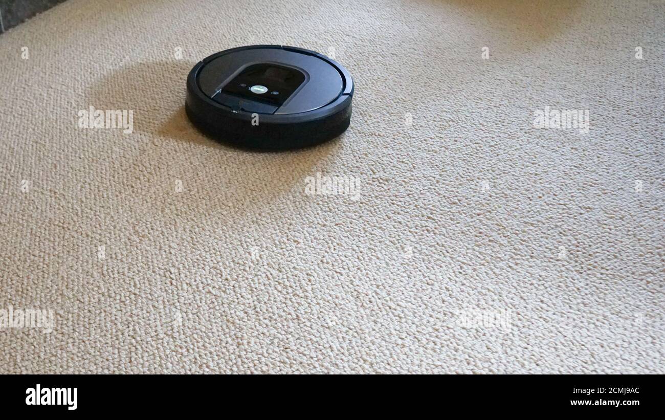 Roomba robotic vacuum on a cream colored carpet making cleaning easier. Stock Photo