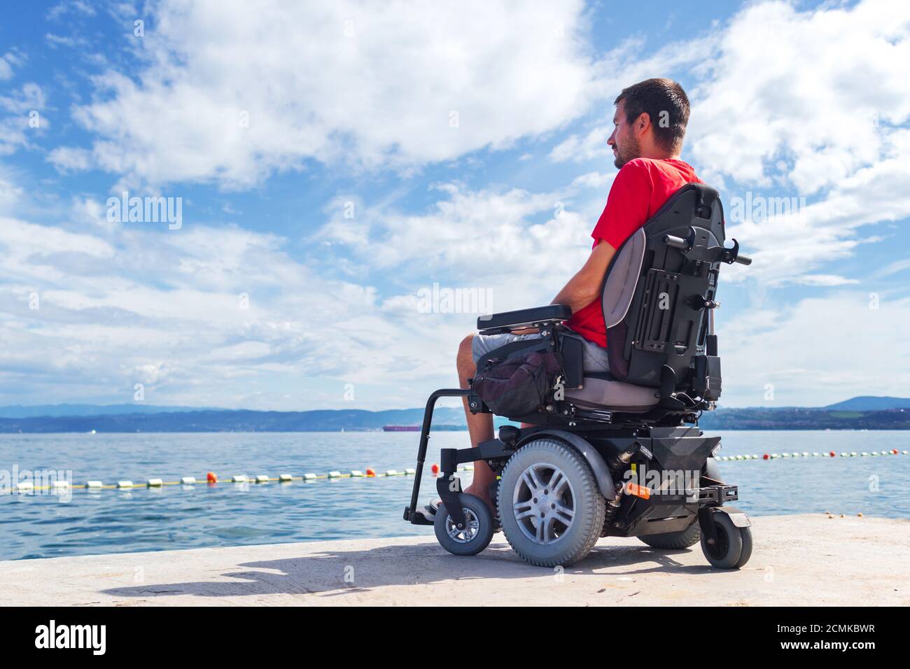 Man with muscular dystrophy on electric wheelchair outdoors looking at