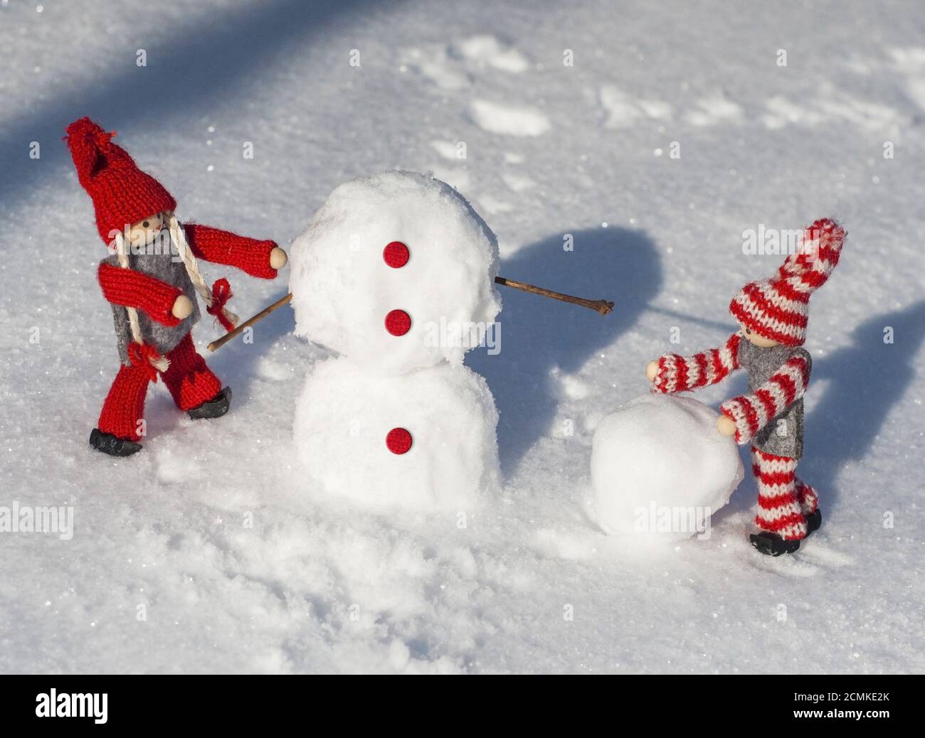 wooden dolls in red knitted clothes roll down snowballs to build a snowman Stock Photo