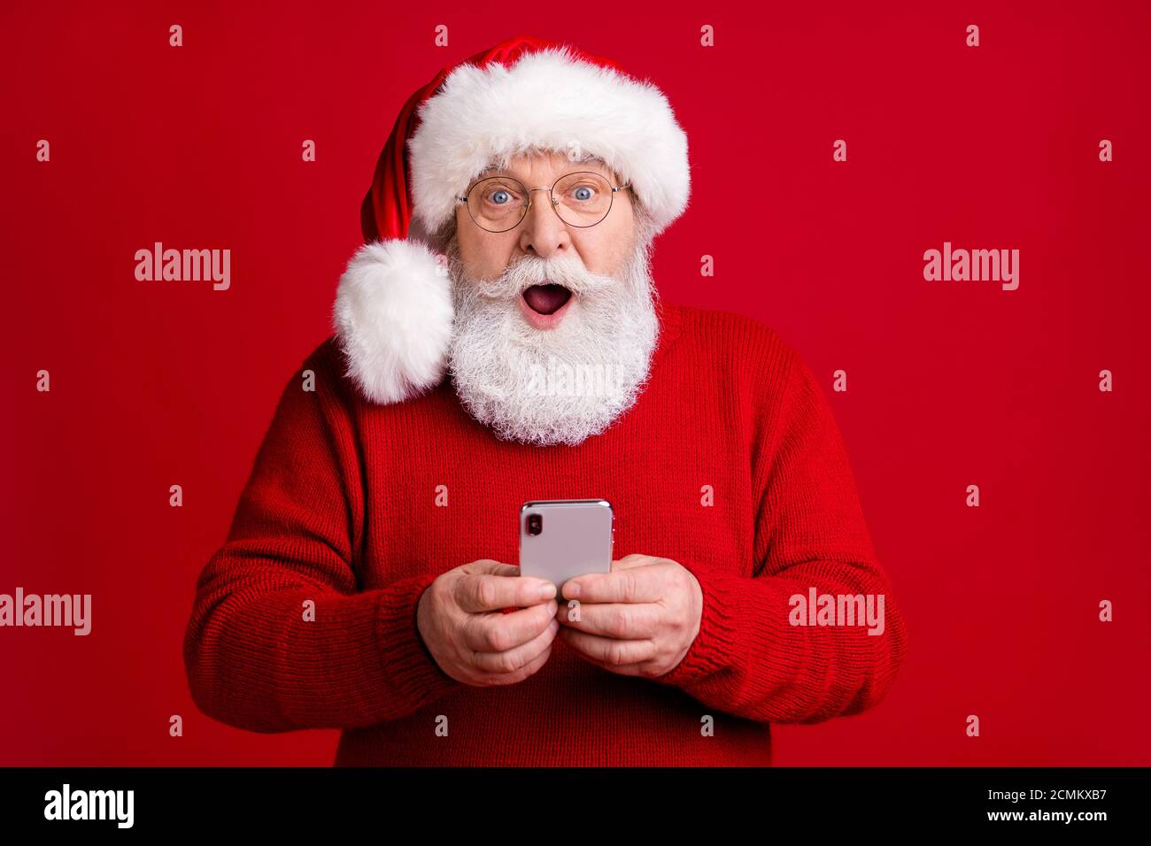 Photo of amazed retired pensioner man in santa claus headwear use smartphone impressed jolly holly x-mas fairy discounts wear sweater jumper isolated Stock Photo